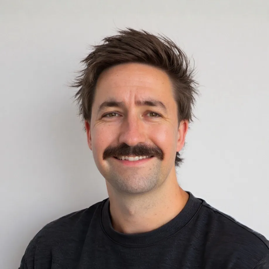 Trystan Conway, a man with brown hair, a moustache and a friendly smile, wearing a black shirt against a plain light background.